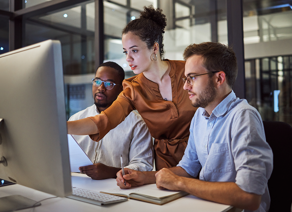 Three colleagues collaborating at a desktop computer.